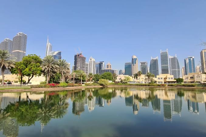 Dubai skyline reflected in a calm lake with palm trees and landscaped gardens